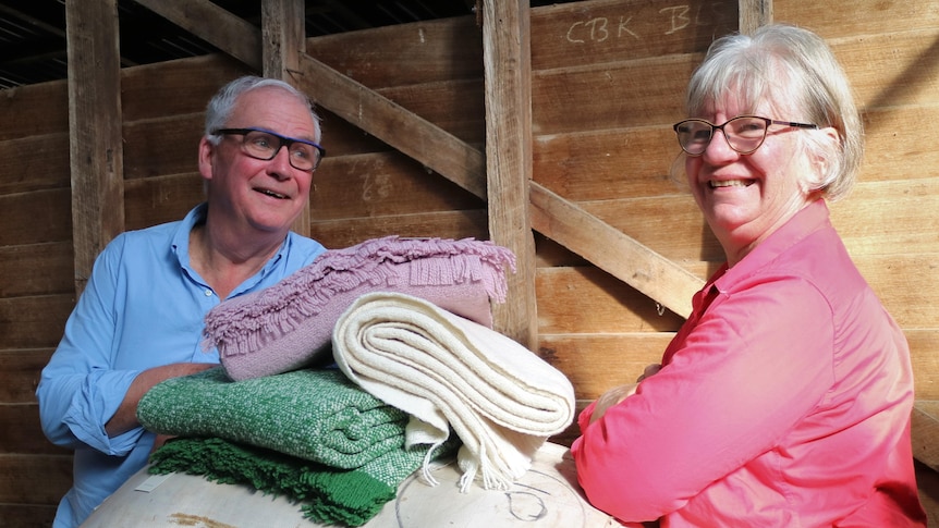 A man and a woman stand between a wool bale, piled with three woollen blankets