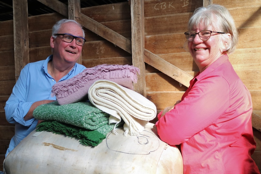 A man and a woman stand between a wool bale, piled with three woollen blankets