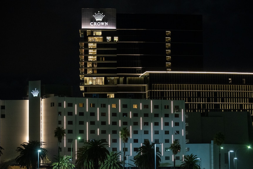 Tall buildings in the dark with lights on with an illuminated sign with the word Crown below a crown symbol.