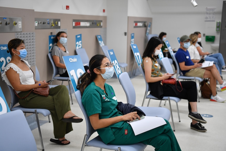 Masked people sit socially distanced.