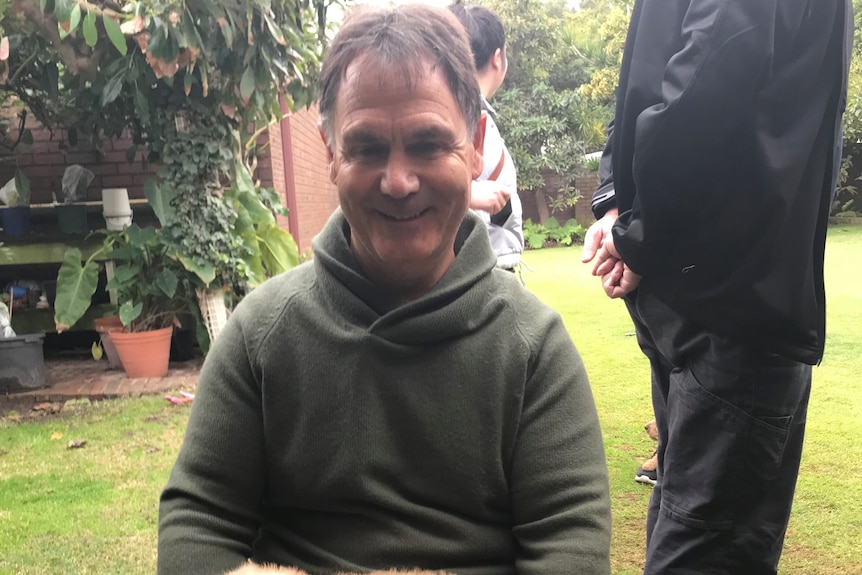 Mr Allen holds a small dog - possibly a puppy - in his lap and smiles.