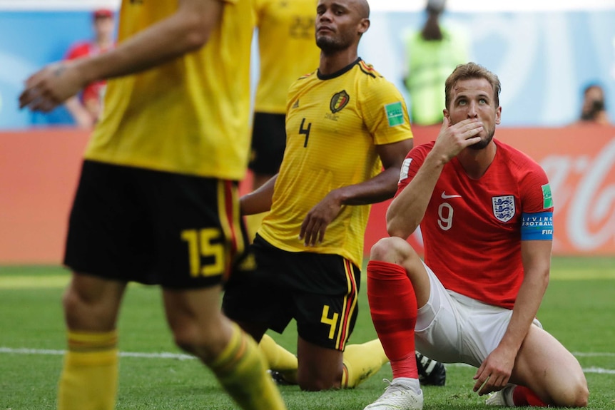 Harry Kane sits on his knees and holds his hand to his mouth