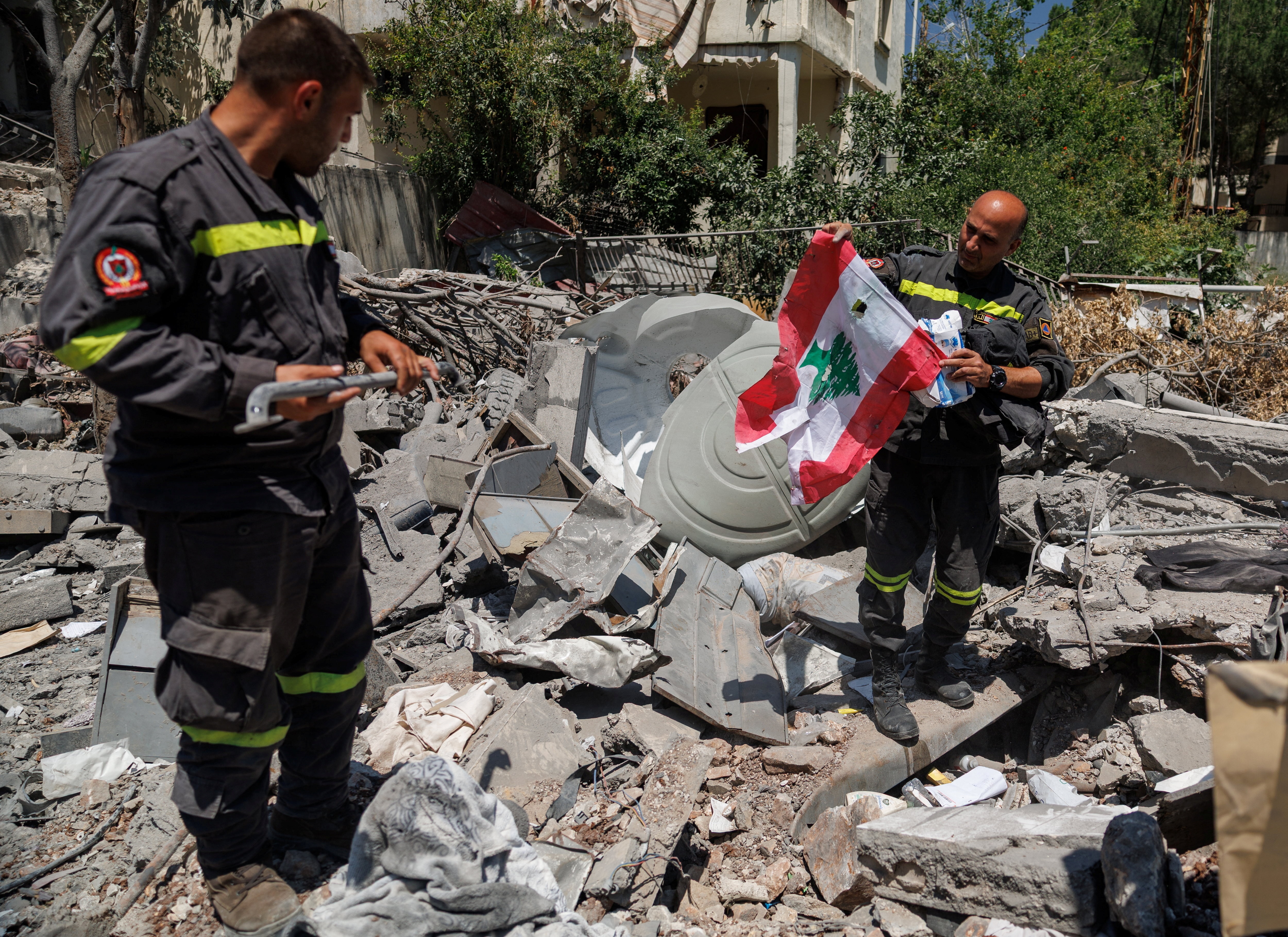 A uniformed officer holding up a Lebanese flag while standing with another worker in a pile of rubble.