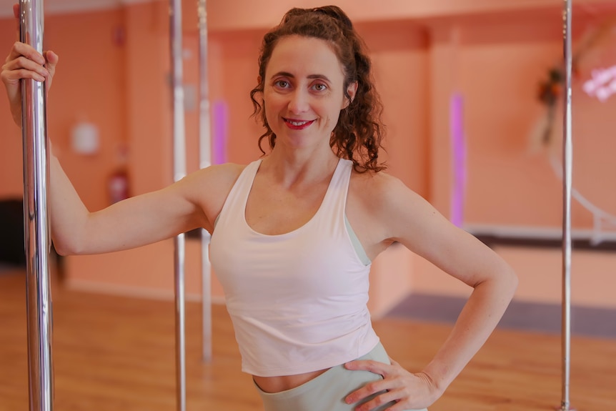 A woman holding on to a dancing pole inside a studio. 