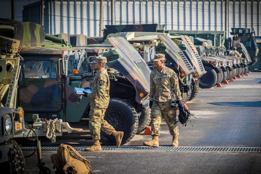 Soldiers walk past a row of military trucks