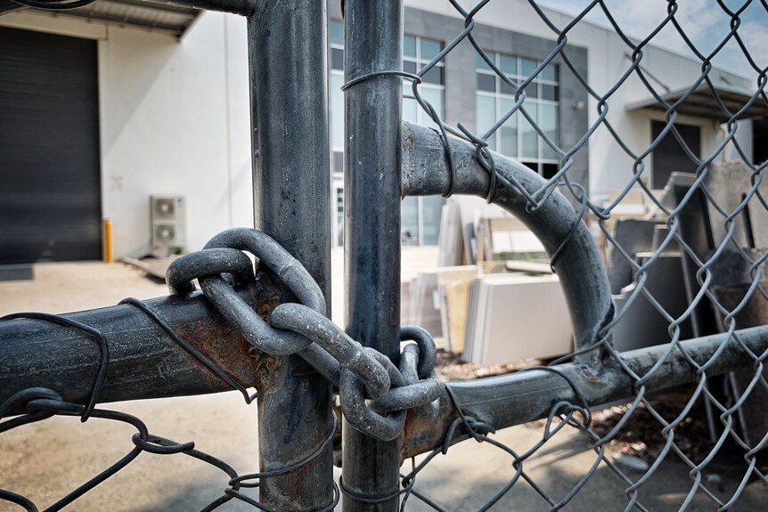 A chain is wound around a closed metal gate in front of a factory.