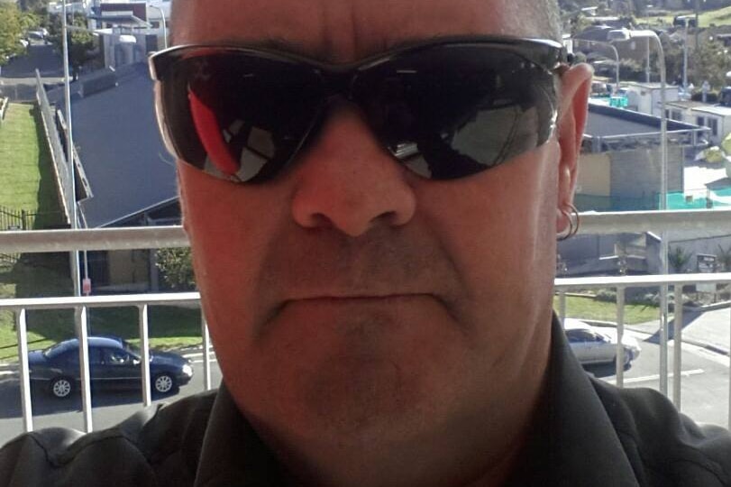 Selfie-style shot of a man wearing dark glasses standing on a balcony.