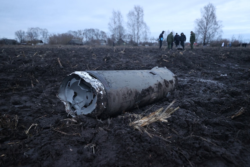 Investigators near a fragment of a munition in the middle of a field.