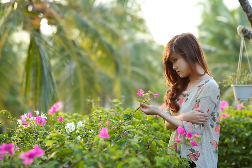 A young woman in a garden looking at a rose