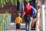The back view of a father holding his child's hand after school pick up.
