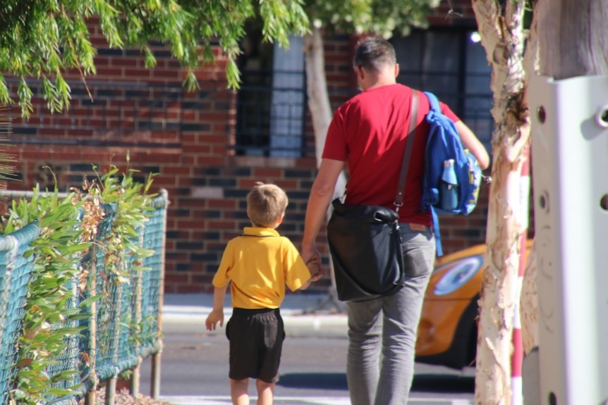 The back view of a father holding his child's hand after school pick up.