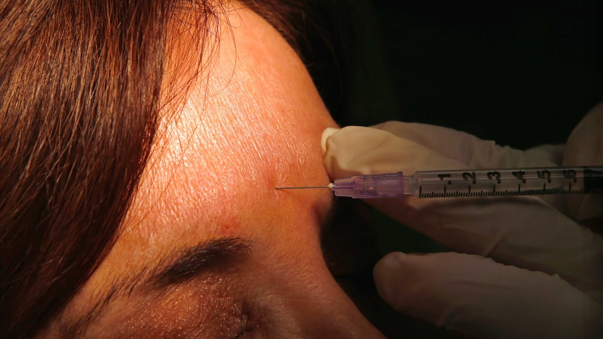 A woman gets botox injected in her forehead