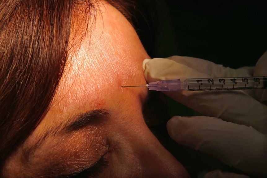 A woman has botox injected into her forehead.