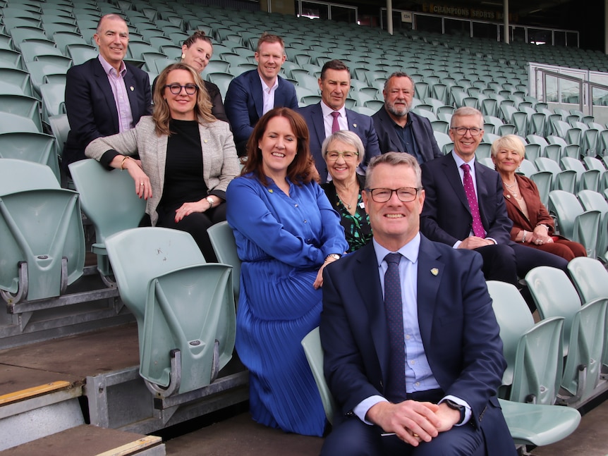 A group of people pose for a photo sitting in stadium seating.