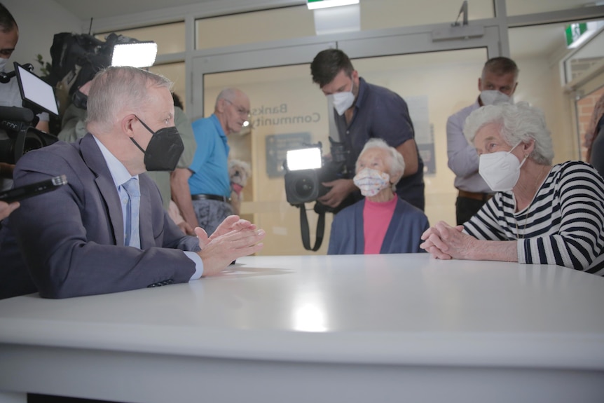 A man wearing a mask sits at a table with elderly women.