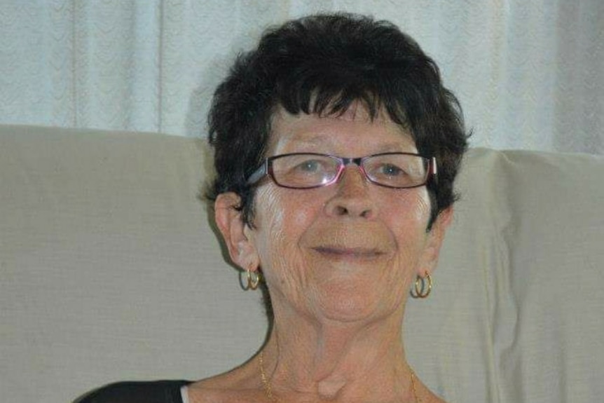 Barbara Francis, wearing glasses and sitting on a couch, smiles at the camera.