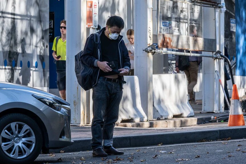 A man wearing a face mask stands in front of a Sydney hospital holding a mobile phone.