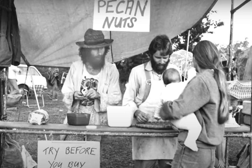 A man with a beard and curly hair sells pecan nuts from a stand.