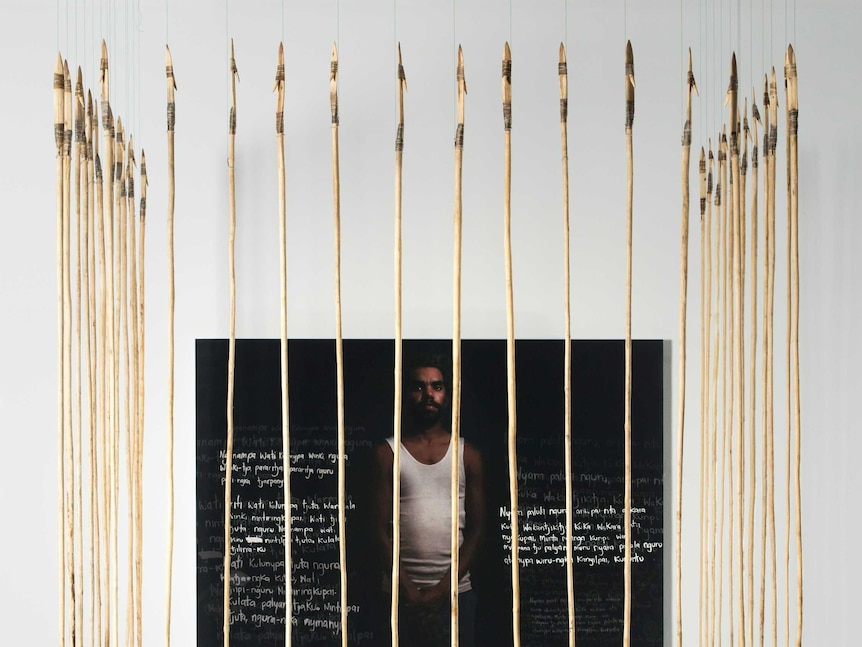 An art installation of a young Indigenous man behind a row of spears.