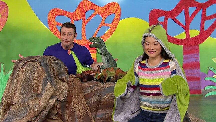 Michelle dressed up as a dinosaur with Teo, surrounded by dinosaur figurines