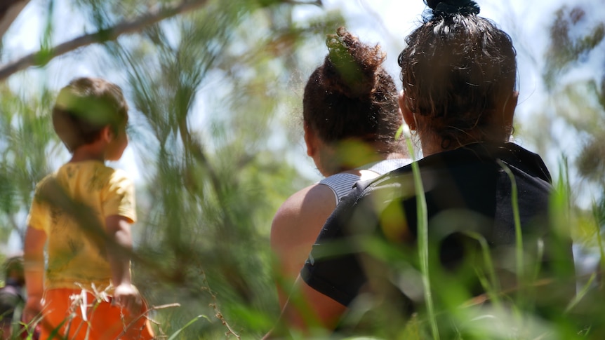 photo from behind two women and a child sitting in long grass