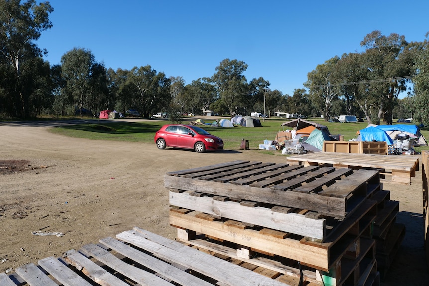 A large stack of pallets with tents and a car in the background.