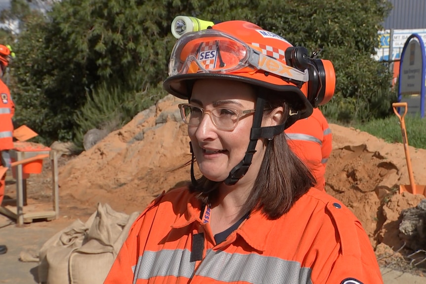 A woman wearing a hard hat and orange high vis stands in front of a large pile of sand