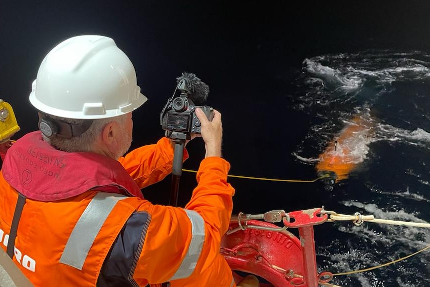 A man points a camera at an orange object in the water