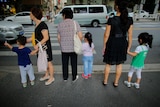 Three older women each hold the hand of a child at a pedestrian crossing