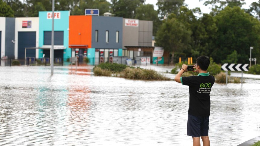 A man takes a photograph of a flooded area near Yatala.