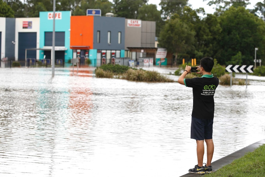 A man takes a photograph of a flooded area near Yatala.