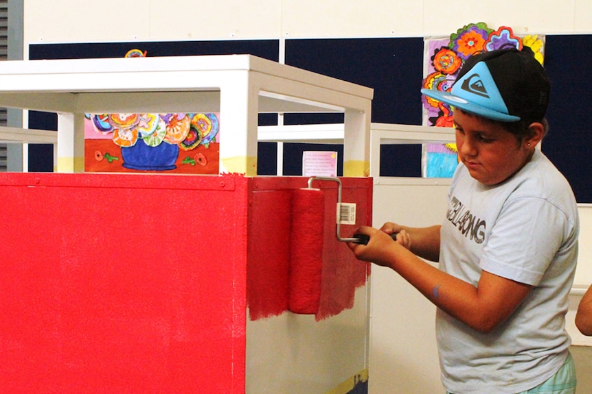 Young boy paints a red base coat on a rubbish bin