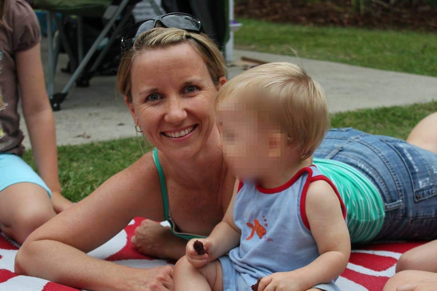 A smiling woman with a small child lies on a picnic blanket