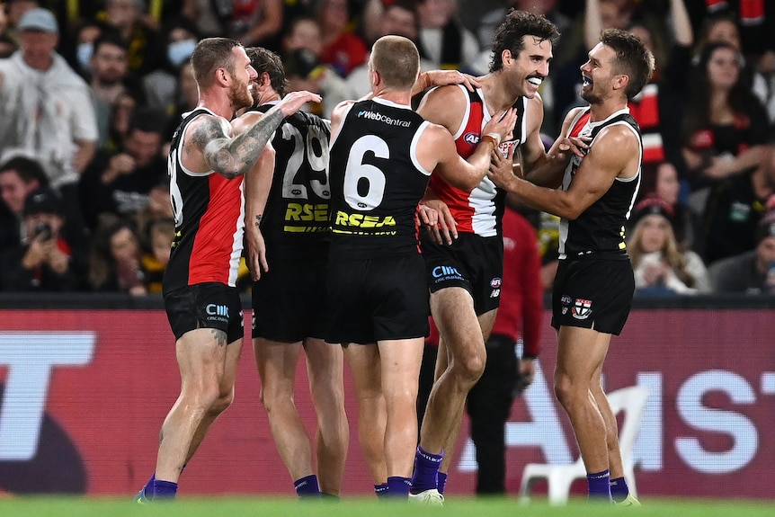 A group of AFL players surround a full-forward after he scores a goal during a match.