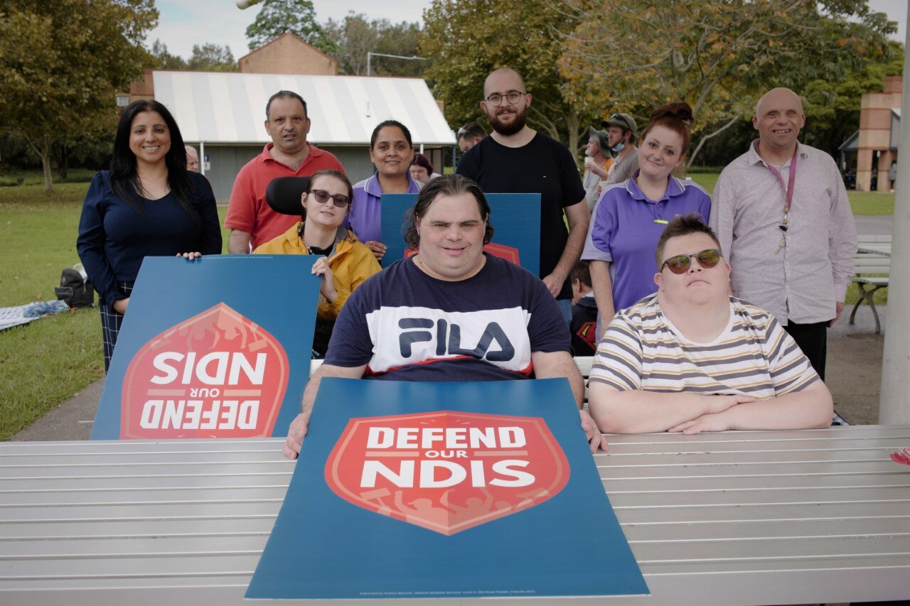 A group of people with disability and their advocates holding signs saying 'Defend our NDIS'