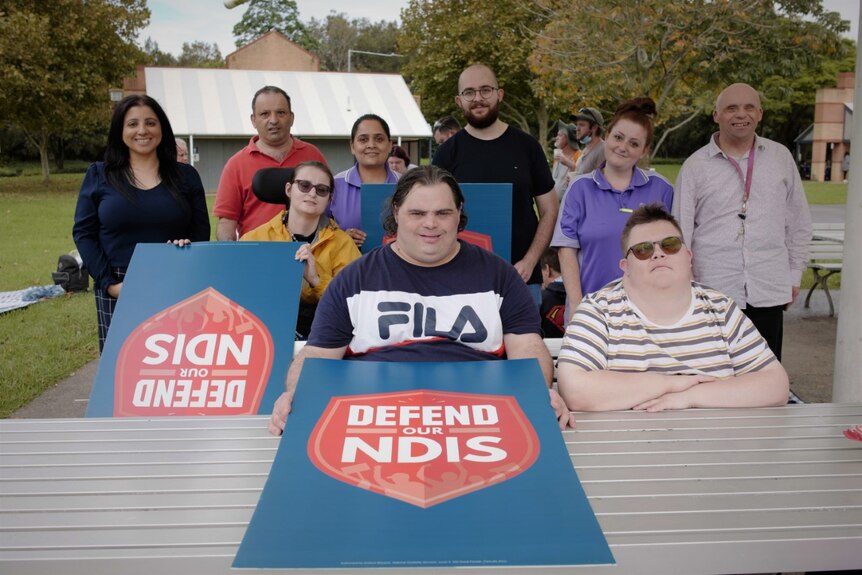 A group of people with disability and their advocates holding signs saying 'Defend our NDIS'