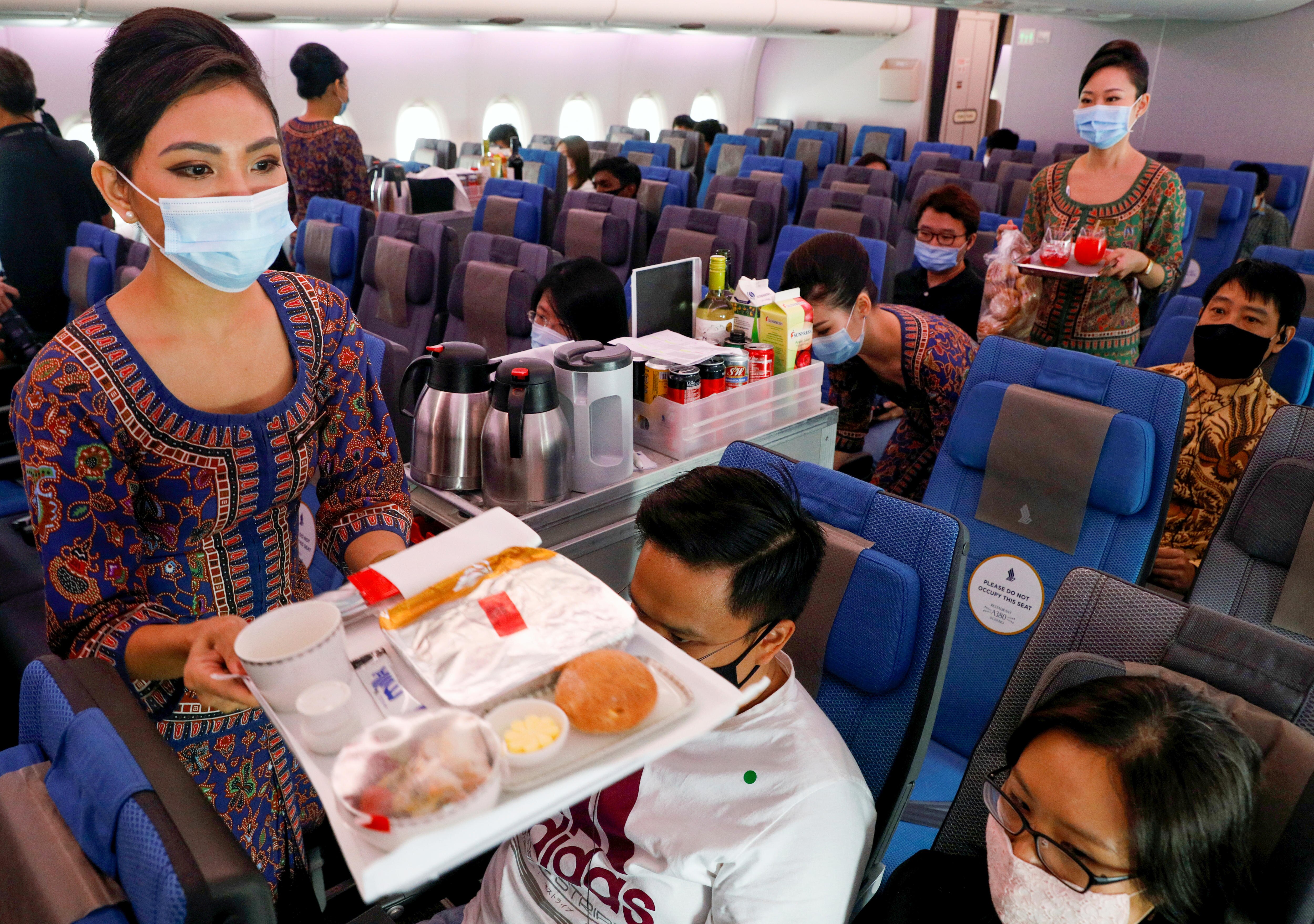 Two flight attendants in masks passing food trays to people in plane seats 