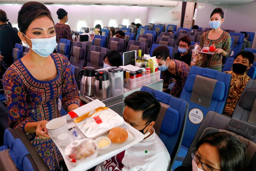 Two flight attendants in masks passing food trays to people in plane seats 
