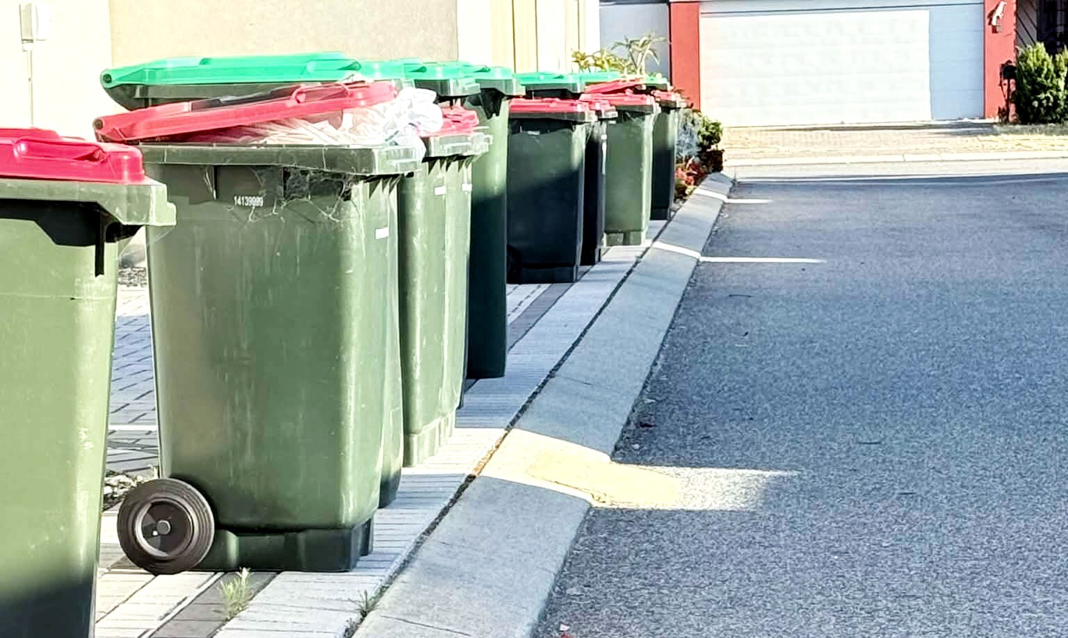 Una fila de botes de basura verdes y rojos desbordantes en una calle