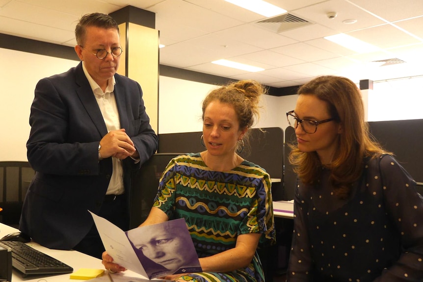 Jill Prior (left) and Elena Pappas (right) look over a woman's shoulder in an office space.