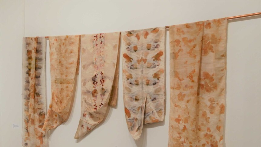 A series of colourful scarves hang on a wall inside an art gallery.