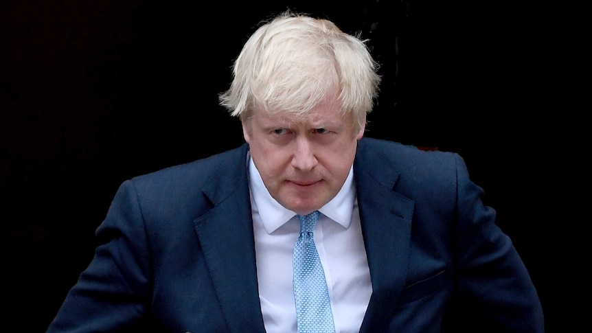 Boris Johnson hunches forward, carrying a folder under his arm, as he walks towards a podium.