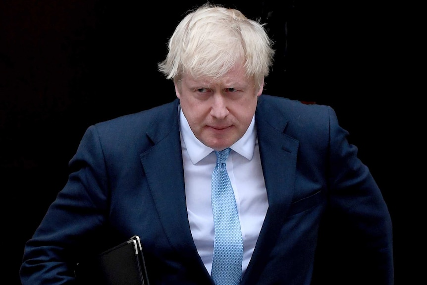 Boris Johnson hunches forward, carrying a folder under his arm, as he walks towards a podium.