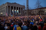 A sea of people wearing variations of blue and yellow are gathered in front of an official building.