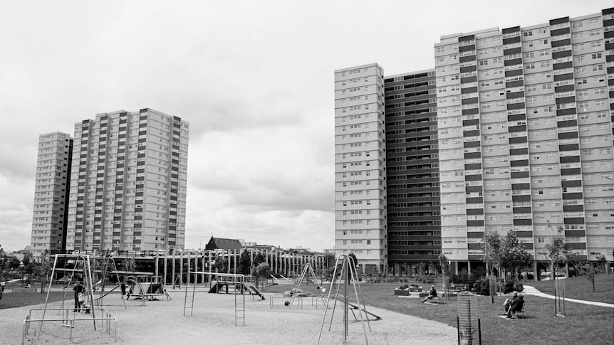 A black and white photo showing two large housing towers in the background, and an empty playground in the foreground