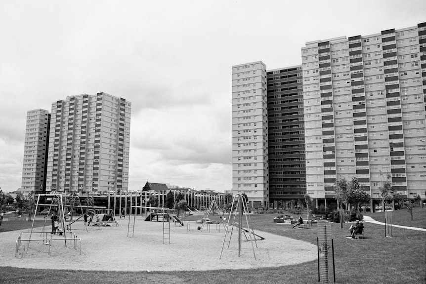 A black and white photo showing two large housing towers in the background, and an empty playground in the foreground