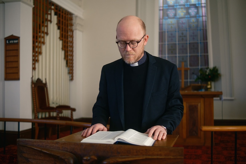 A priest reads from a notebook.