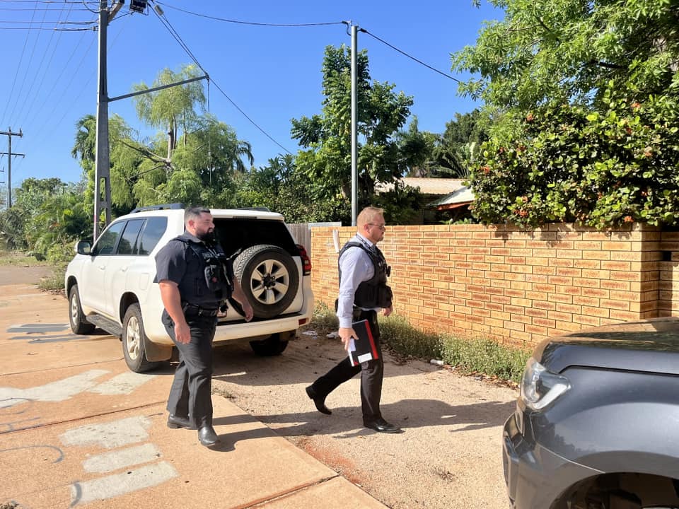Two police walk towards the gate in a brick fence