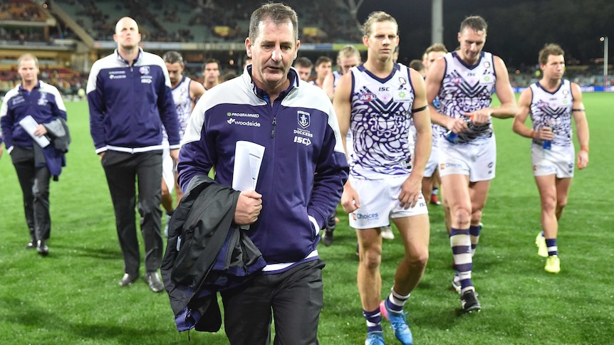 Coach Ross Lyon walks in front of some of his Fremantle Dockers players and fellow coaches on Adelaide Oval.