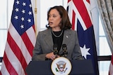 Kamala Harris speaks at a podium with Australian and US flags behind. Anthony Albanese, Antony Blinken are next to her
